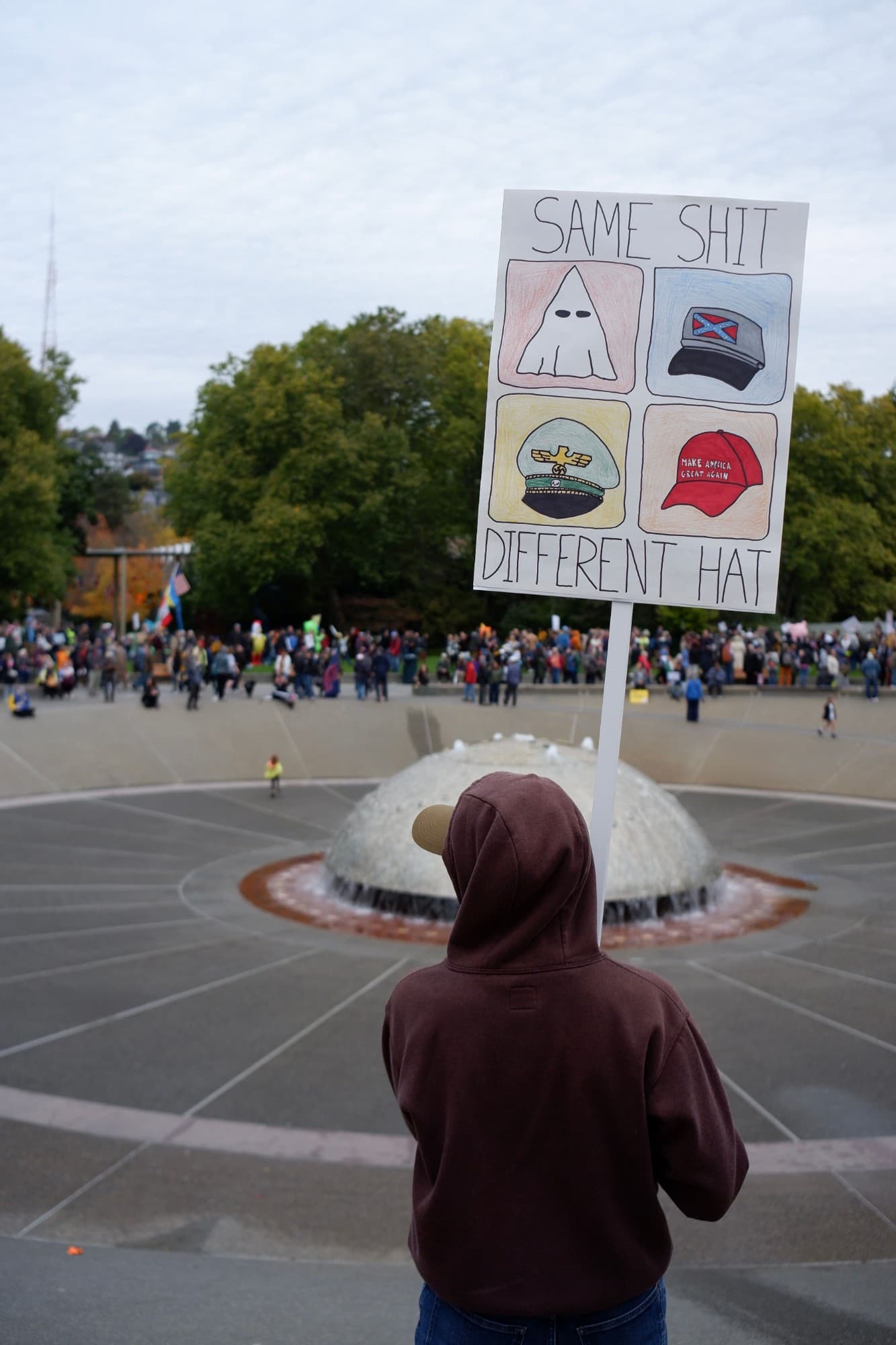 A protester holding a hand-drawn sign reading: Same shit, different hat